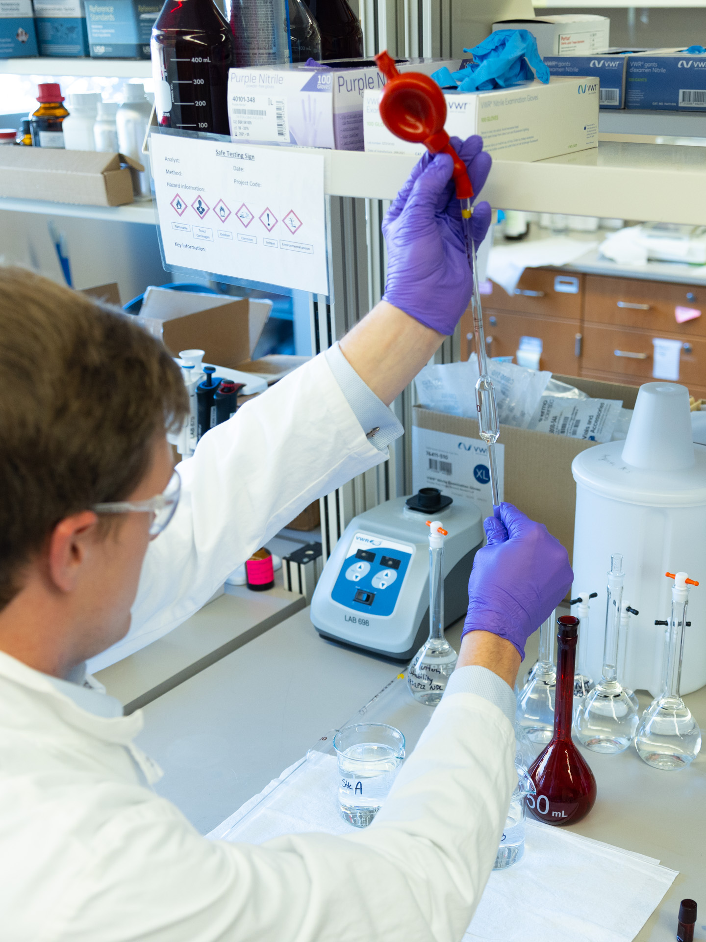 A man in a labcoat and other personal with protective equipment holds a long pipette in a lab at the Bioscience and Technology Business Incubator in Lawrence, KS.